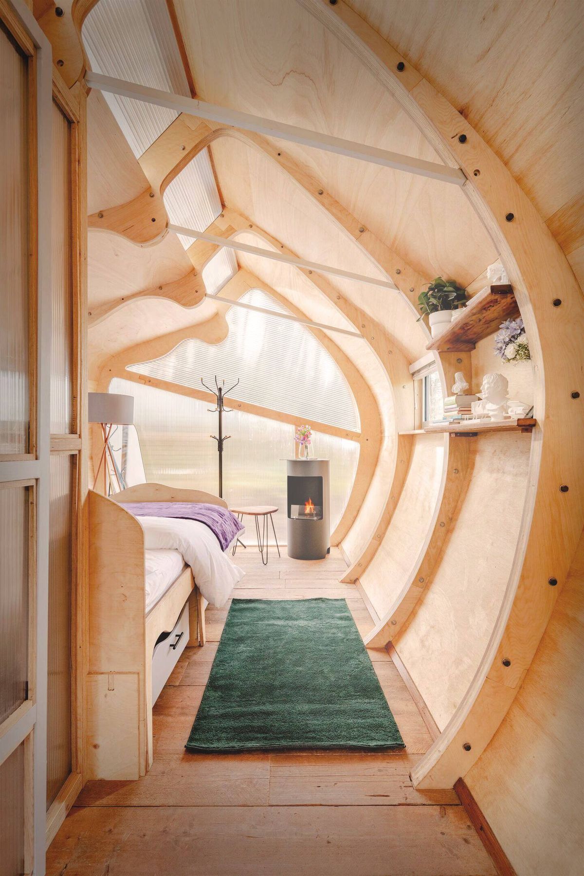 Intérieur en bois aux courbes organiques, poêle allumé et lumière traversante